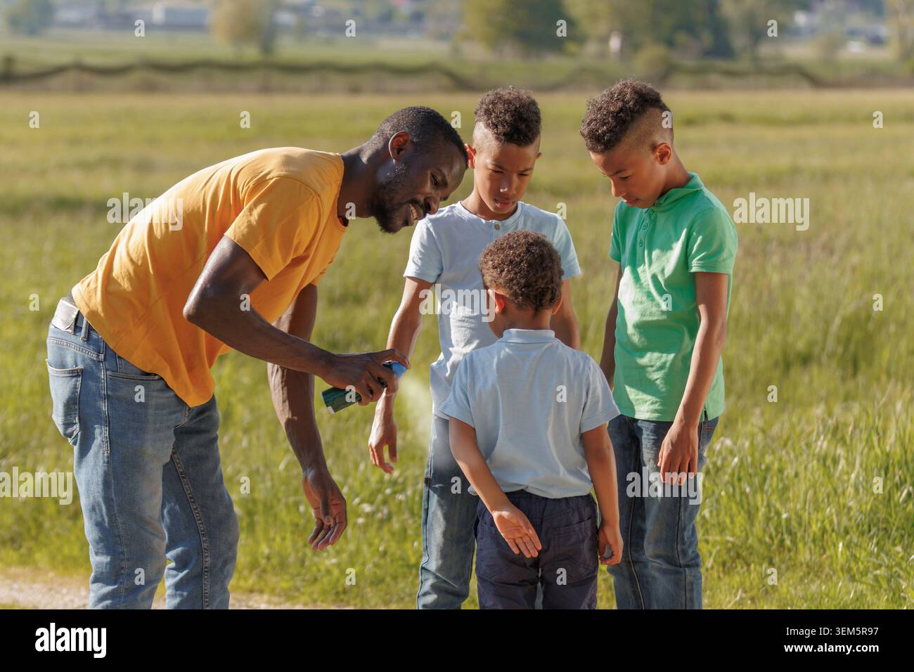 Vater wendet an einem Sommertag in der Natur Insektenspray auf seine Kinder an, um sie vor Mücken zu schützen und die Zeit der Familie zu genießen. Stockfoto
