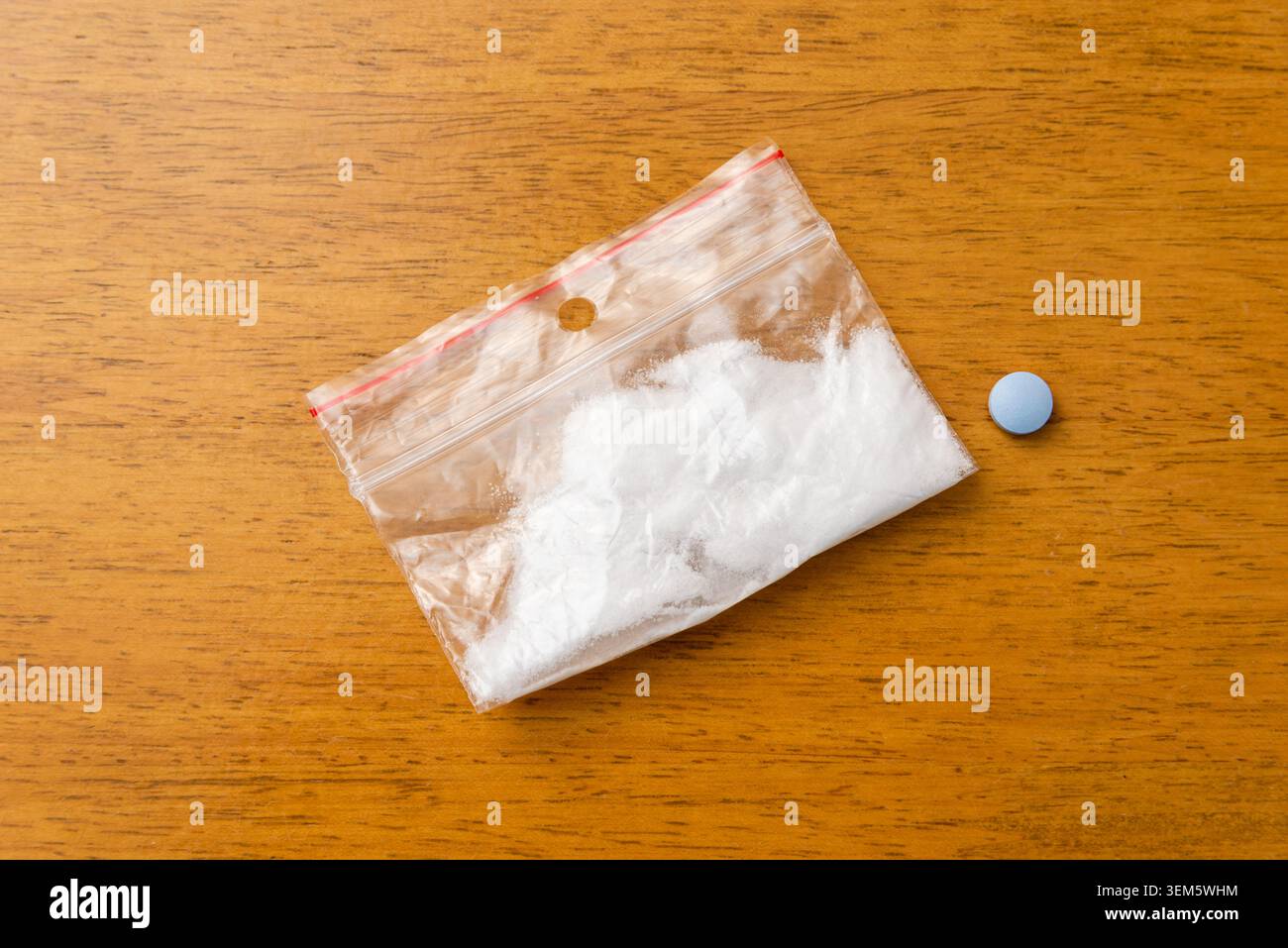 Transparenter Beutel mit weißem Betäubungspulver neben einer einzelnen blauen Ecstasy-Tablette, Drogenmissbrauchskonzept. Kleiner Plastikbeutel mit Reißverschluss mit weißem Pulver und Stockfoto