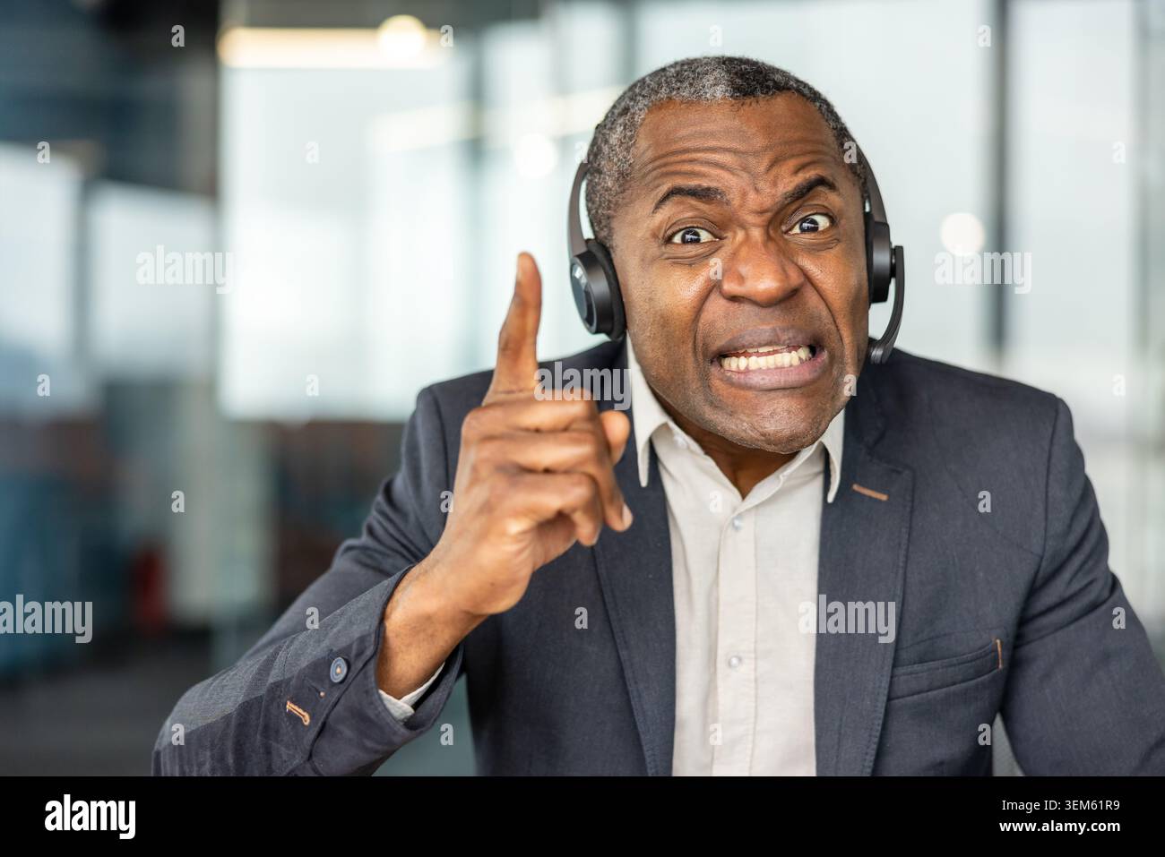 Reife Person, die in einem Callcenter arbeitet, ein Headset trägt und einen frustrierten Ausdruck zeigt, während sie mit dem Finger zeigt, was Wut, Stress oder ein schwieriges Gespräch darstellt Stockfoto