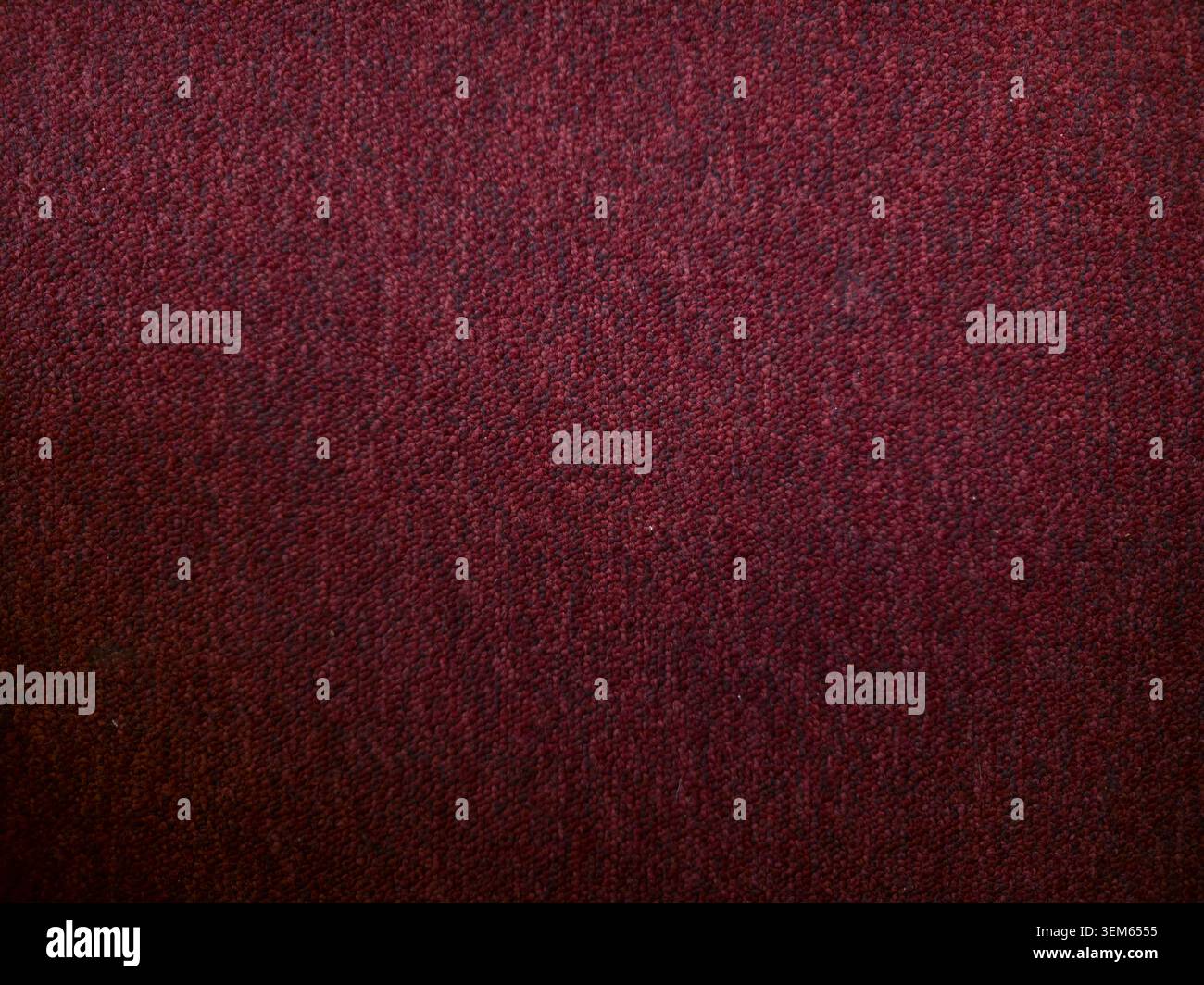 Dunkelroter Teppichhintergrund. Nahaufnahme aus bordeauxfarbenem Stoff, Teppich oder Polstermaterial mit gewebtem Muster und dezenten dunklen Vignettenkanten. Stockfoto