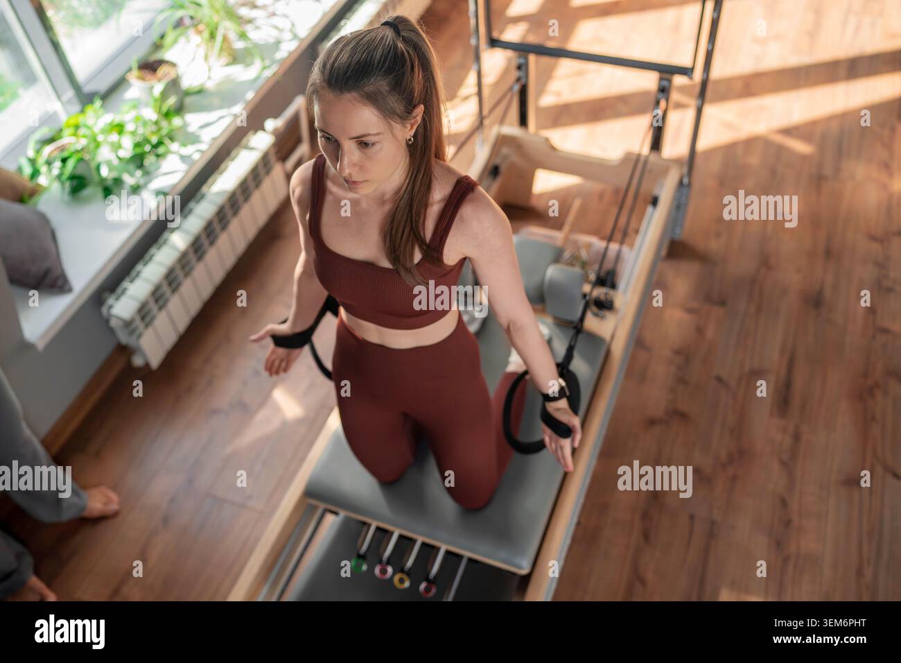 Frau, die Pilates-Übungen auf dem Pilates-Reformer für Brust, Arme Bizeps und Rückenmuskeln macht und sich auf Flexibilität, Kraft und Kontrolle konzentriert Stockfoto