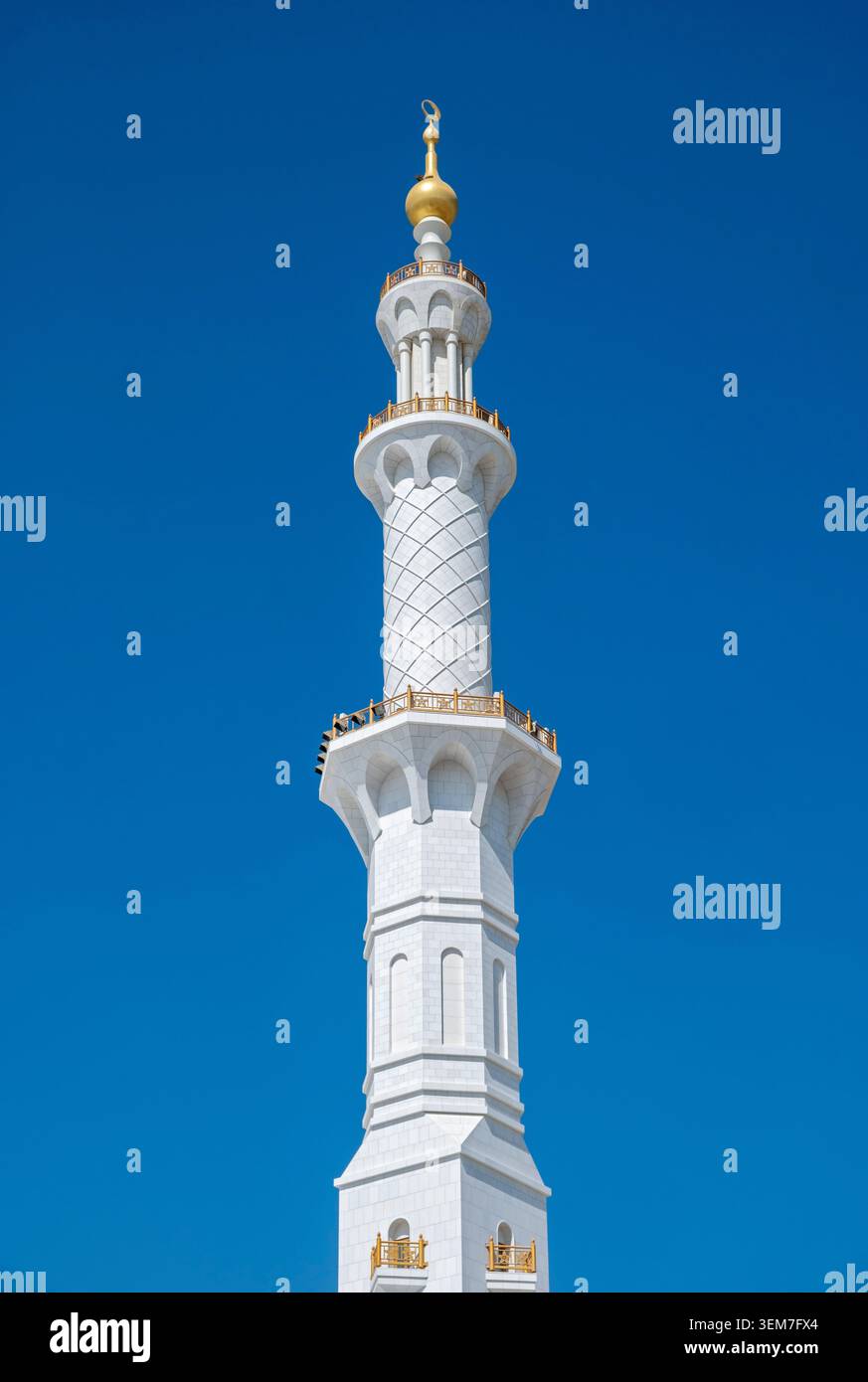 Ein detaillierter Blick auf den verzierten Minarettturm aus weißem Marmor mit goldenen Balkonen unter einem hellblauen Himmel, Scheich-Zayed-Moschee, Abu Dhabi, VAE Stockfoto