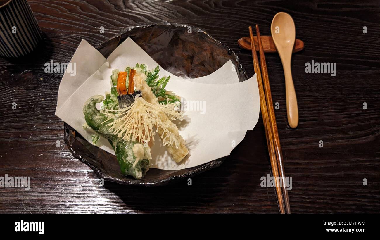 Knuspriges Gemüsetempura von Shojin Ryori mit frittierten Beilagen und frischem Grün, wunderschön auf einem rustikalen dunklen Teller angeordnet. Stockfoto