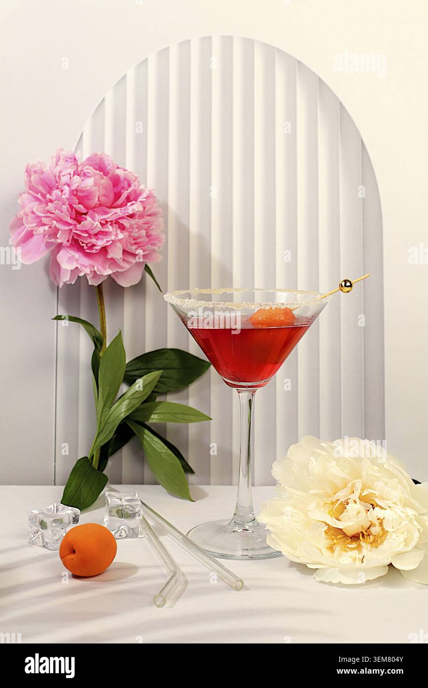 Modernes Stillleben mit rosafarbenem Martini, Sommer-alkoholischer Cocktail mit Aprikose für Party und Pfingstrosen auf elegantem modernem Hintergrund, minimalistisches Konzept für Stockfoto