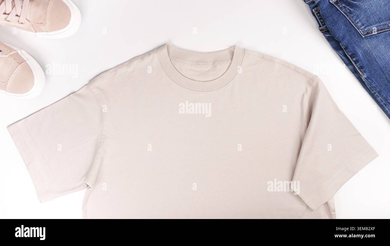 Beigefarbenes Unisex-T-Shirt im Lay-up-Look auf weißem Hintergrund. Vorderansicht von oben T-Shirt, Snikers, Jeans und Copy Space. Mockup T-Shirt und Sommer. Templ Stockfoto