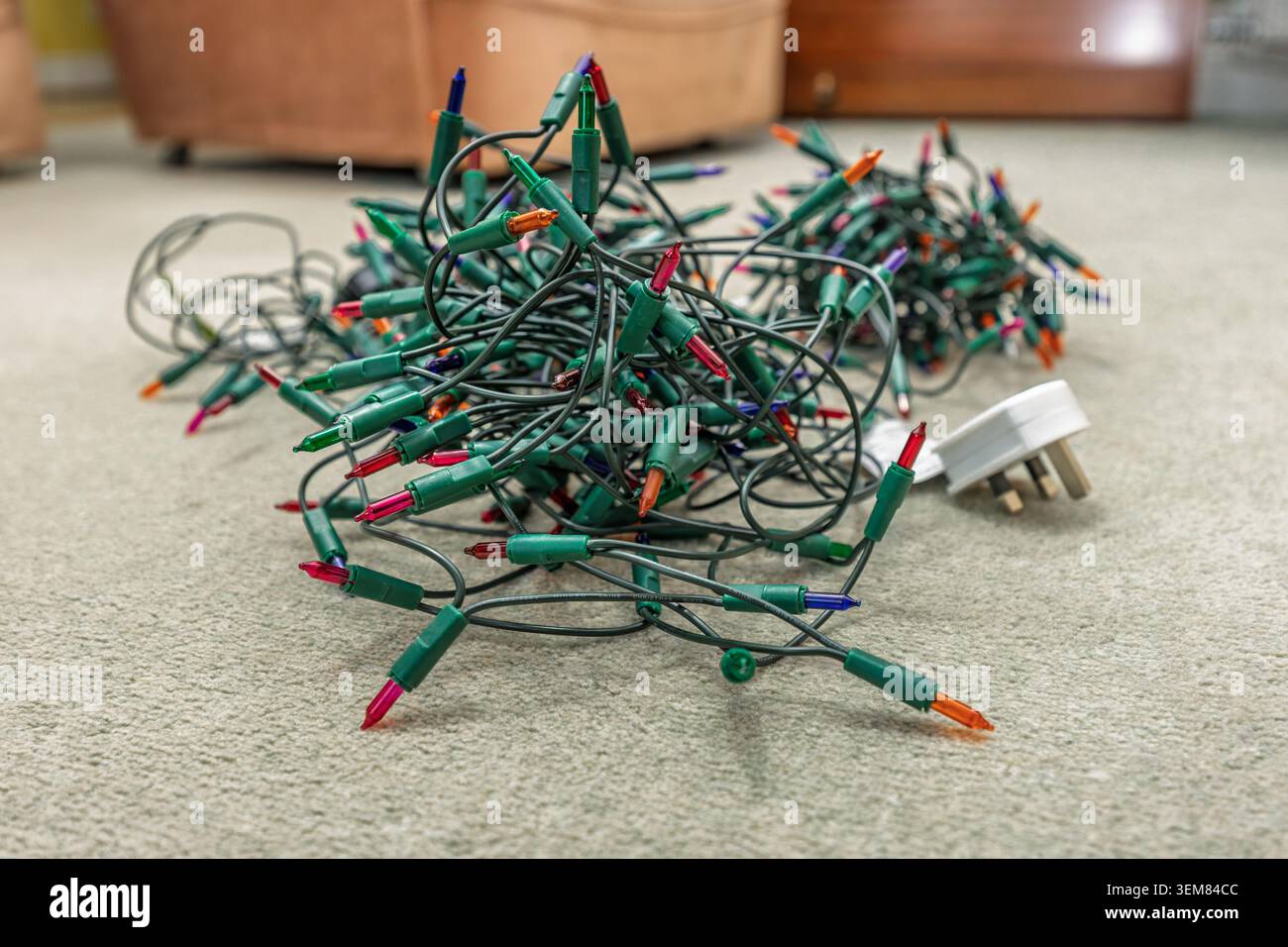 Verwickelte Lichterkette mit farbigen Weihnachtsbaumlichtern auf einem Wohnzimmerteppich, bevor die festliche Weihnachtsdekoration zu Hause stattfindet Stockfoto