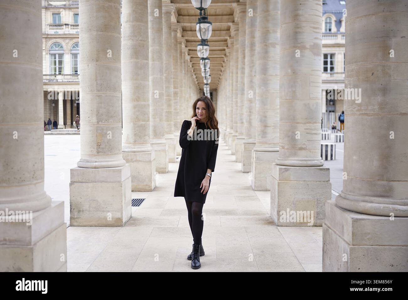 Selbstbewusste Frau in schwarzem Kleid, die durch die elegante Steinkolonnade des Palais Royal in Paris, Frankreich, geht. Stilvolle urbane Lifestyle-Szene Stockfoto