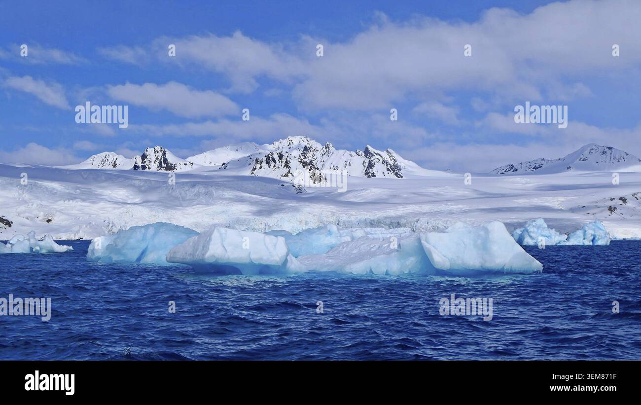 Blick auf einen türkisfarbenen Eisblock, der in den kalten Gewässern eines Fjords im norwegischen Archipel von Svalbard driftet, vor dem Hintergrund der schneebedeckten Kulisse Stockfoto