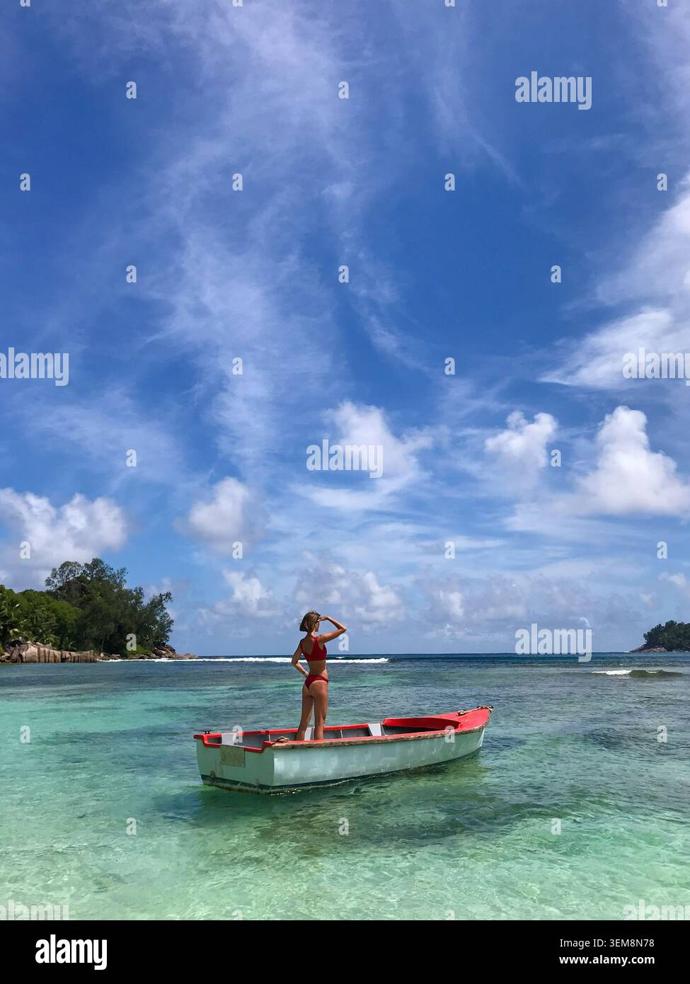 Schlanke Frau von hinten in einem roten Bikini, anmutig auf einem traditionellen Fischerboot, das im flachen kristallklaren türkisfarbenen Wasser schwimmt. Stockfoto