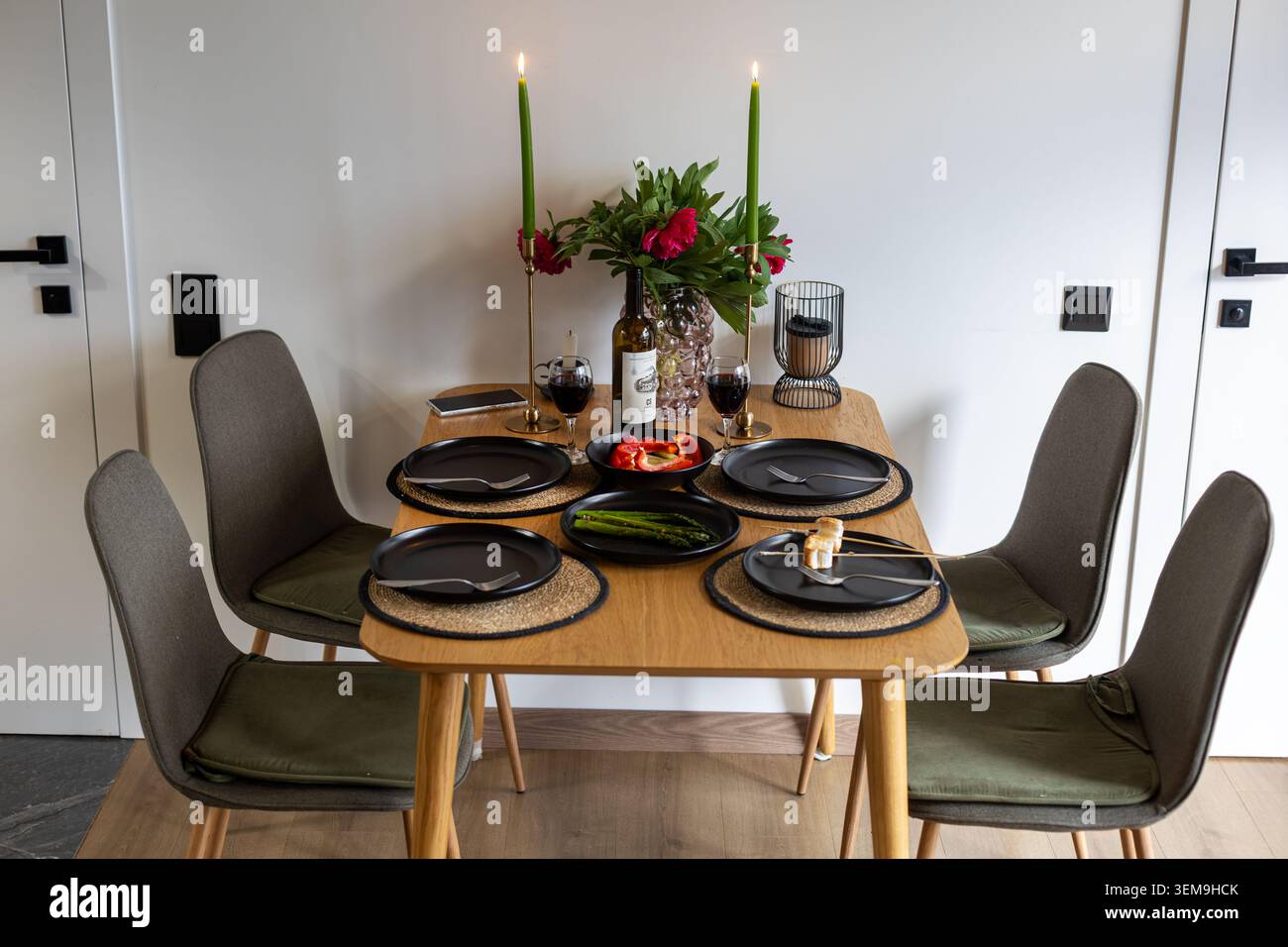 Esstisch mit Kerzenlicht für vier Personen. Moderner Esstisch mit Kerzen, Wein, Blumen, schwarzen Tellern und Gemüse für eine intime Atmosphäre Stockfoto