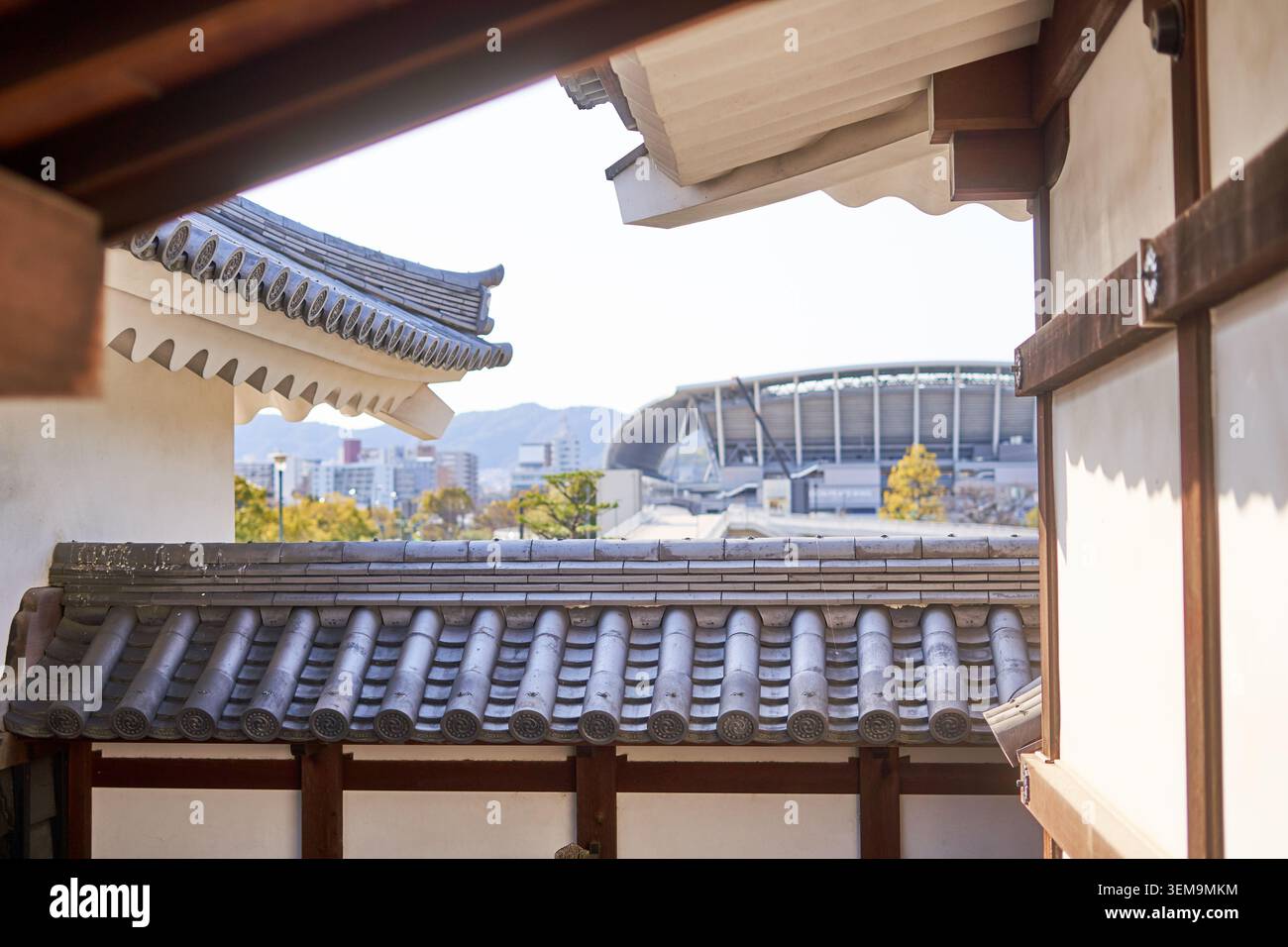Eine Ansicht durch traditionelle japanische architektonische Elemente, die geschwungene graue Ziegeldächer und Holzbalken zeigen, die eine moderne Stadionstruktur einrahmen Stockfoto