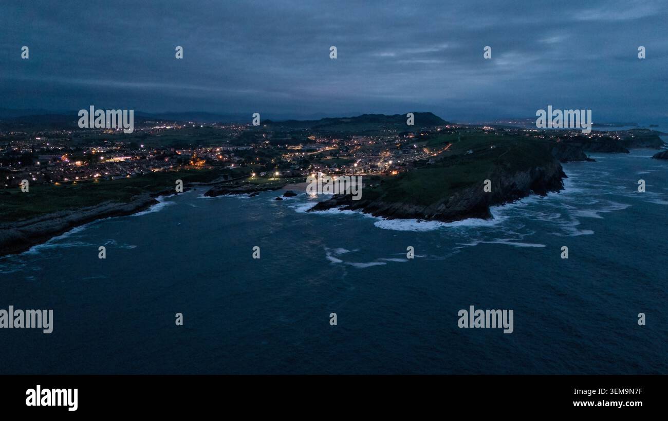 Aus der Vogelperspektive auf die felsige Küste und die Lichter der Stadt in der Abenddämmerung Stockfoto