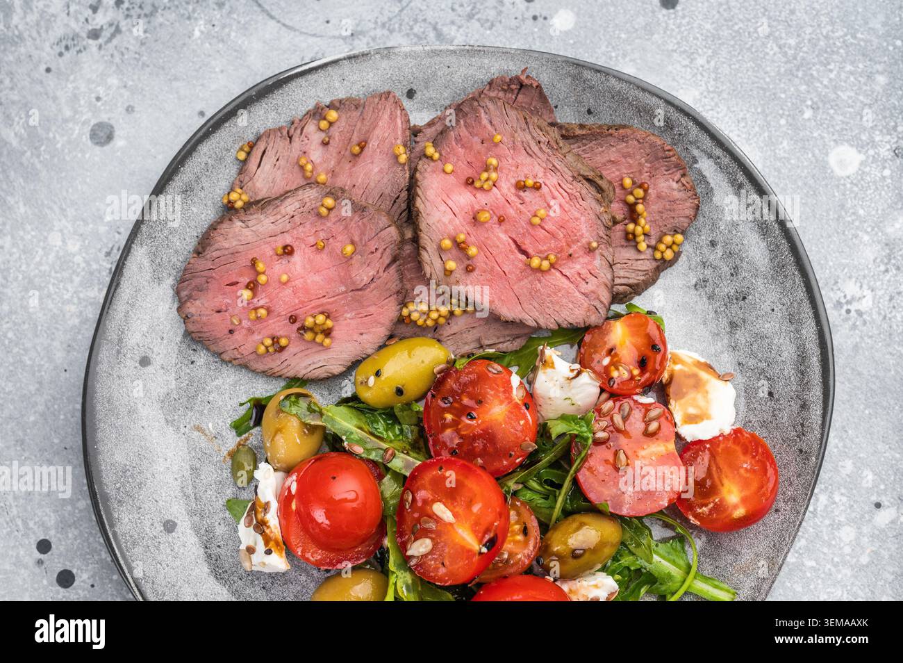 Gesunder Roastbeef-Salat mit medium rare Rindfleischscheiben, Gemüse, Tomaten, Oliven und frischem Käse, heller Hintergrund, Flat Lay Stockfoto