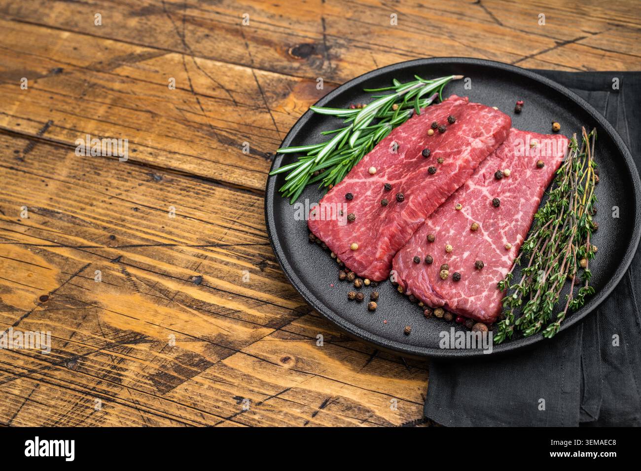 Rohe marmorierte Wagyu-Rindersteaks mit Rosmarin und Thymian in einer Eisenpfanne. Rotes Gourmet-Fleisch auf Holztisch mit Blick. Stockfoto