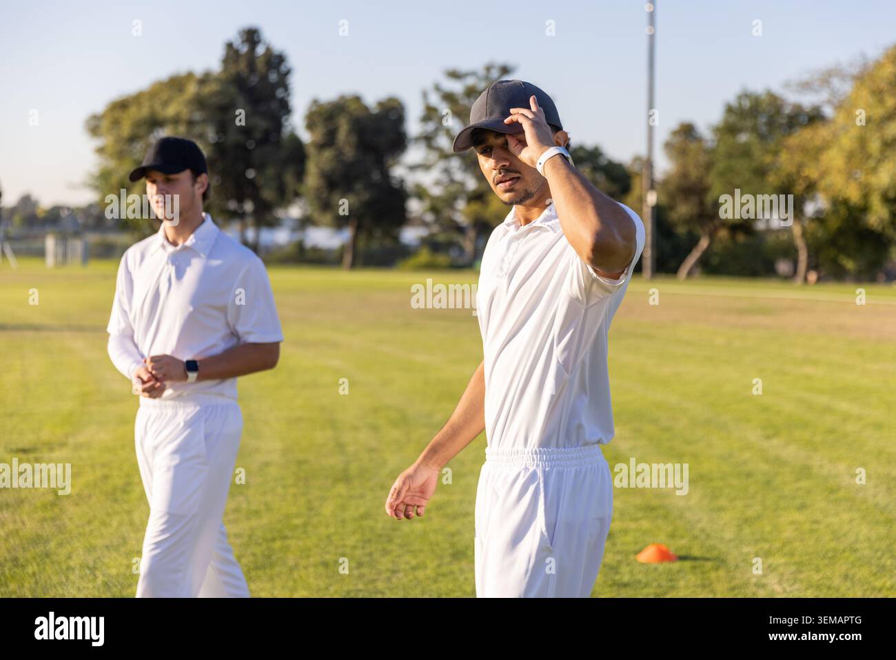 Verschiedene männliche Spieler in weißen Uniformen stehen auf dem Spielfeld, verstellbare Kappe durch orangefarbenen Kegel, Kopierraum Stockfoto