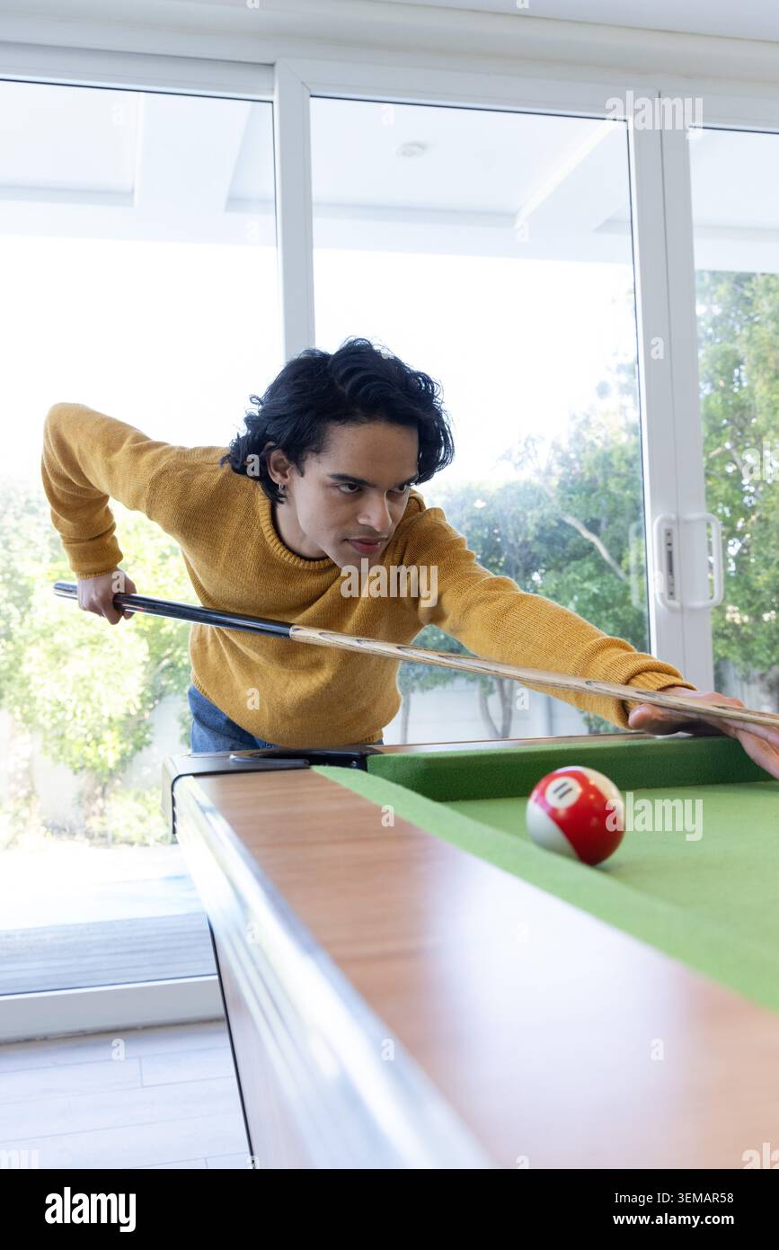 Mann, der sich zu Hause über den Billardtisch beugt und mit dem Stichstock auf den rot gestreiften Ball zielt Stockfoto
