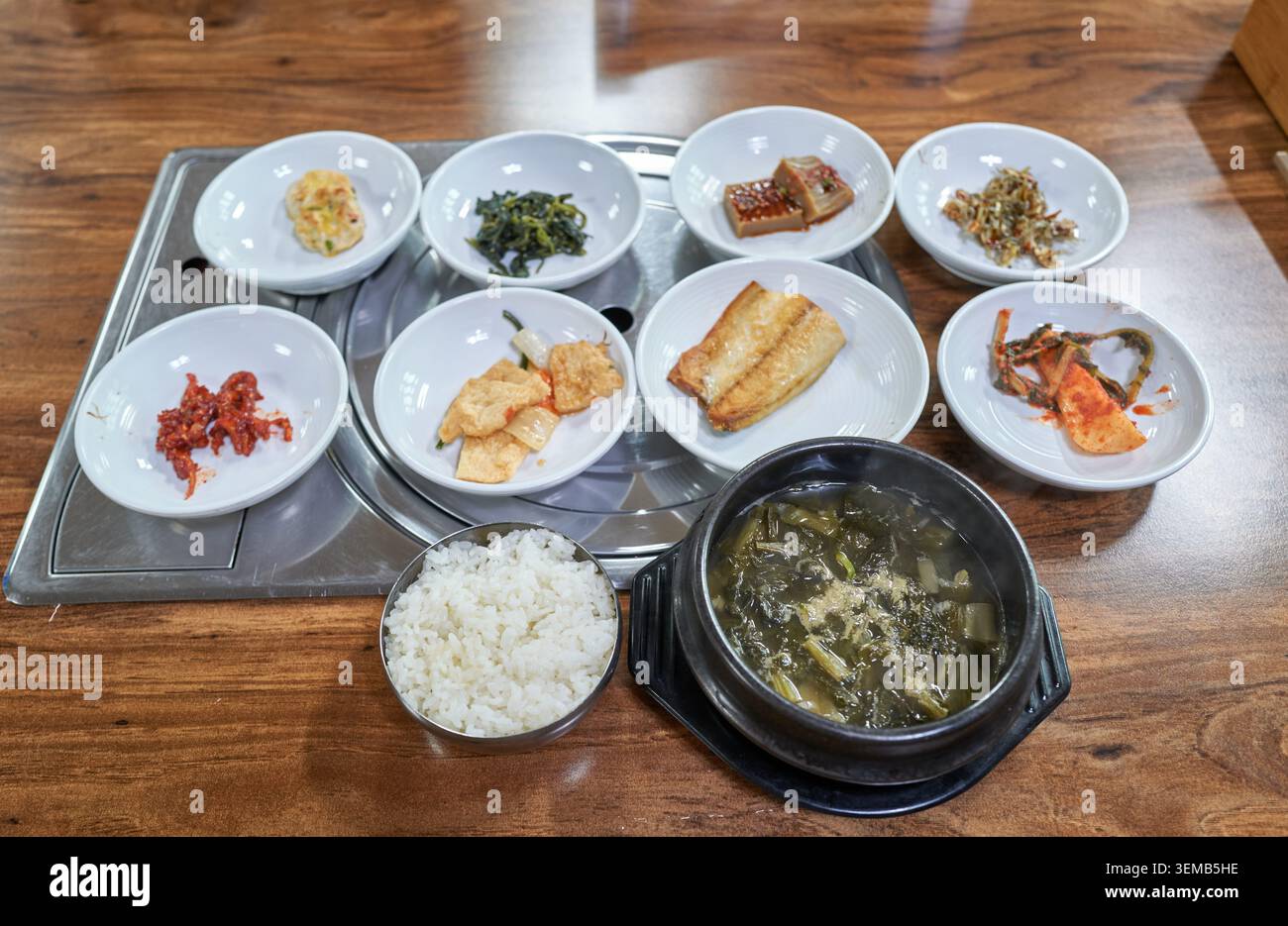 Traditionelles koreanisches Gericht mit getrockneter Rettich-Grünsuppe in einem Tontopf, weißem Reis und verschiedenen authentischen Beilagen auf einem Holztisch. Stockfoto