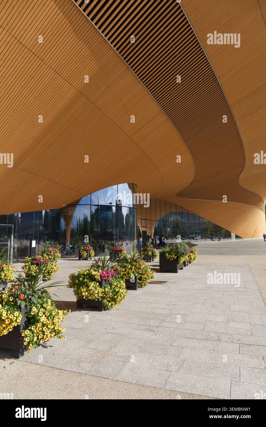 Abgewinkelter Blick unter einem goldenen, geschwungenen Baldachin mit Blumenpflanzen und gepflastertem platz im Sommerlicht. Stockfoto