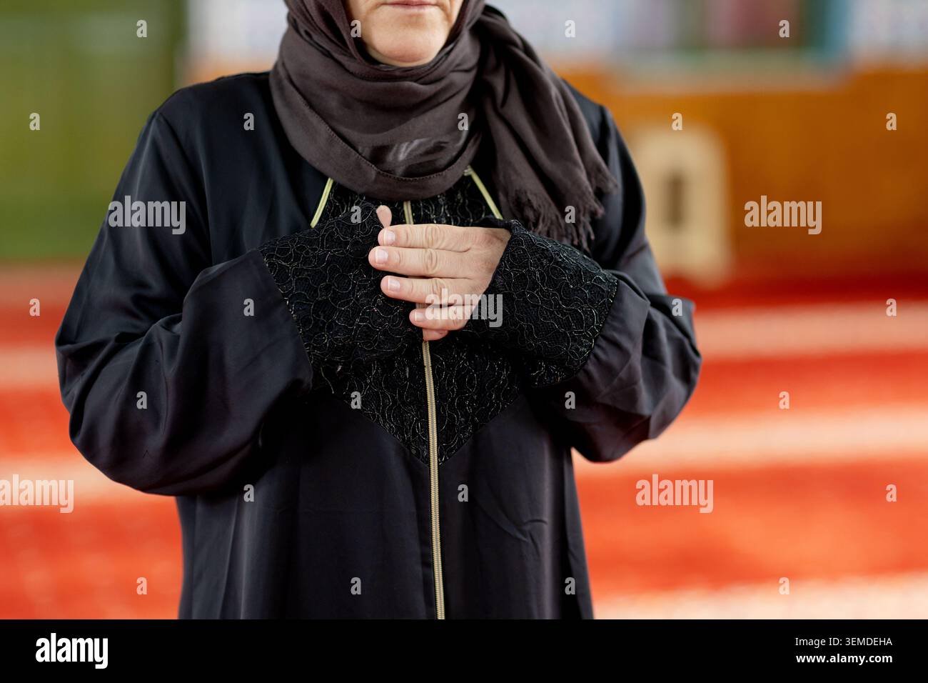 Nahaufnahme einer muslimischen Frau in Abaya und Hijab, die in einer Moschee mit gefalteten Händen im Gebet steht und Glauben, Hingabe und stille spirituelle Reflexion zeigt Stockfoto
