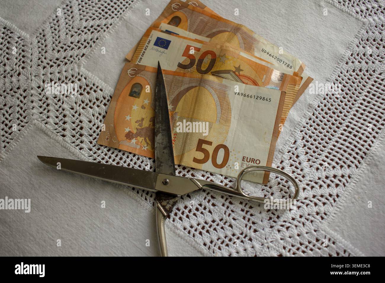 Eine Kopfaufnahme von 50 Euro-Banknoten unter einer scharfen Metallschere, die auf metaphorische Weise steigende Preise, Haushaltskürzungen und Ökono veranschaulicht Stockfoto