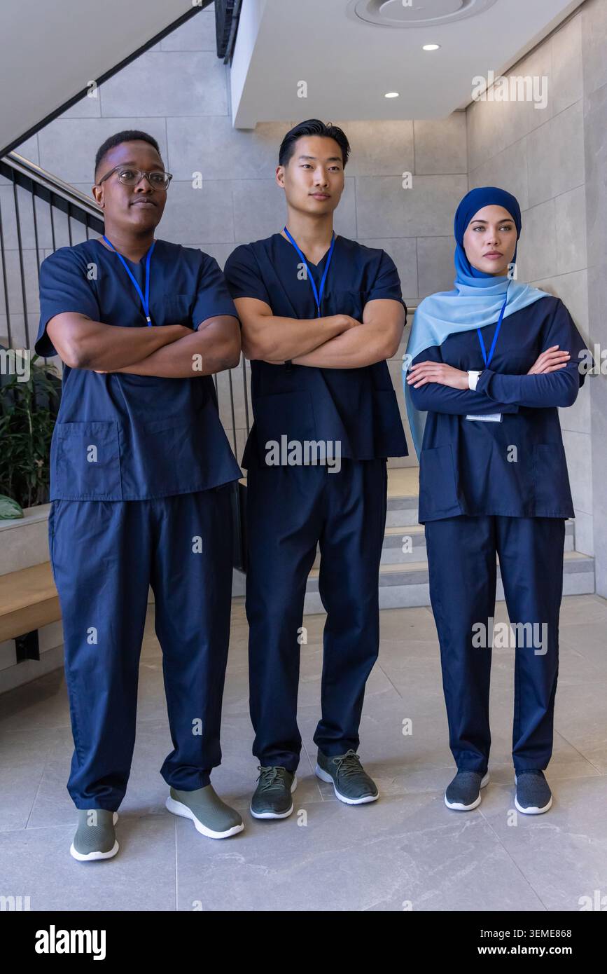 Ein vielfältiges Gesundheitsteam steht an der Treppe in der Lobby in marineblauen Peelings und blauen ID-Schlüsselbändern Stockfoto