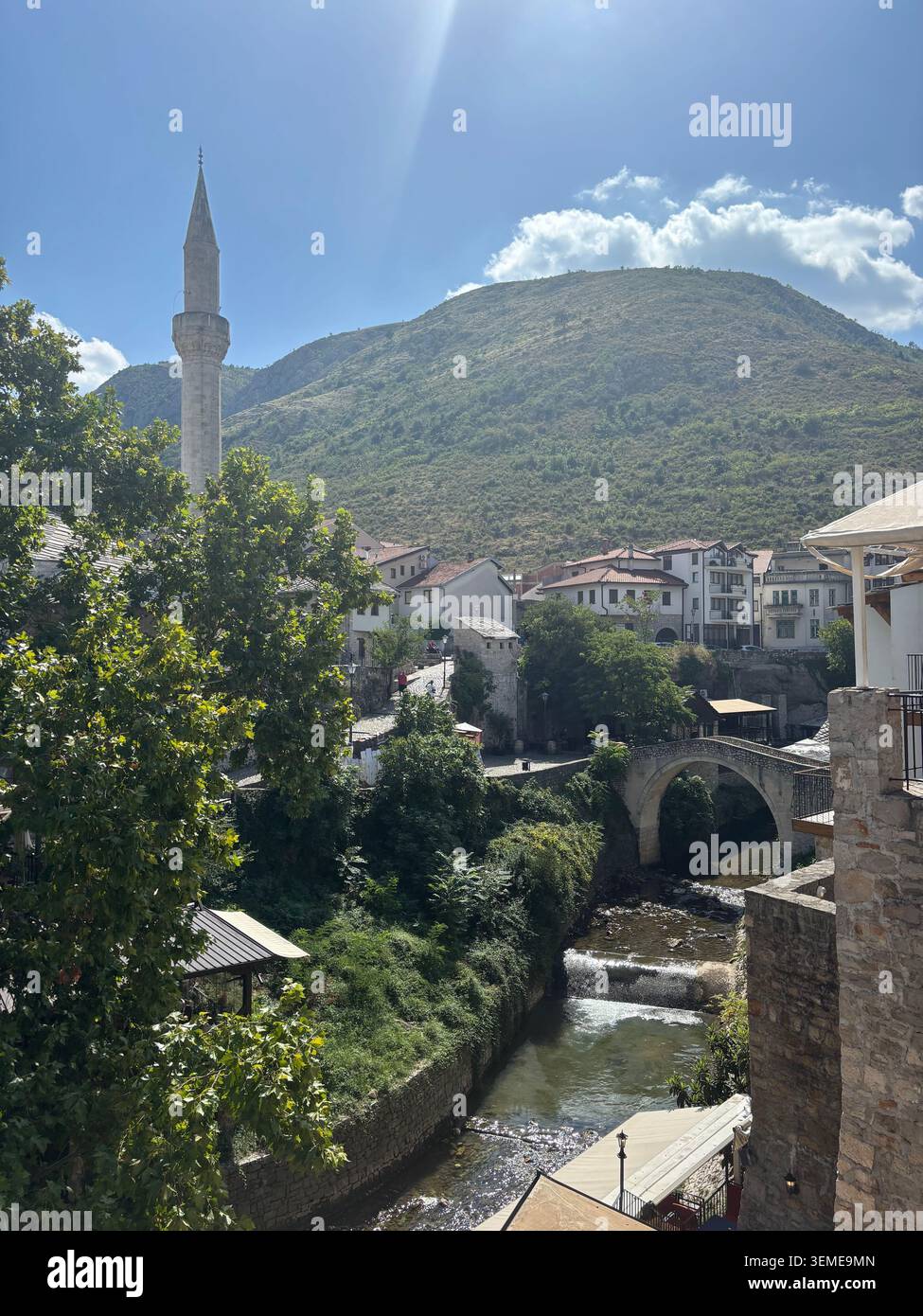 Blick auf die Altstadt von Mostar in Bosnien und Herzegowina, mit einem Moschee-Minarett, einer Steinbrücke, einem Fluss und einer Bergkulisse. - Smartphone-aufgenommenes Stockfoto