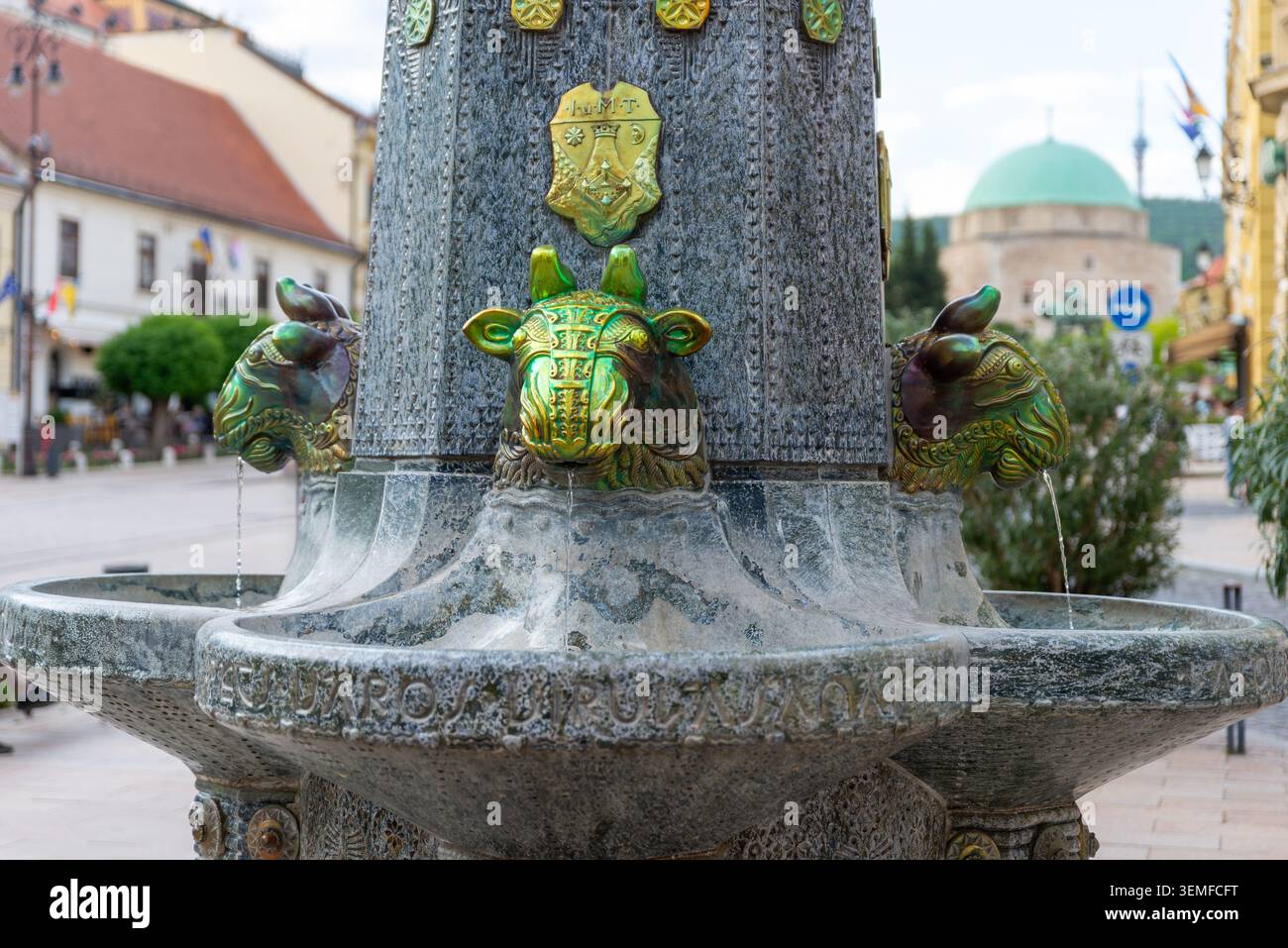 Pécs, Ungarn – 1. Mai 2026: Detail des historischen Brunnens von Zsolnay mit der Moschee von Pascha Qasim im Hintergrund Stockfoto