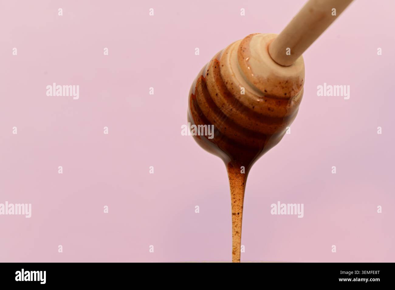 Nahaufnahme von Honig, der von einem hölzernen Löffel tropft, vor einem weichen rosa Hintergrund. Studio-Food-Foto mit Platz für Werbung. Stockfoto