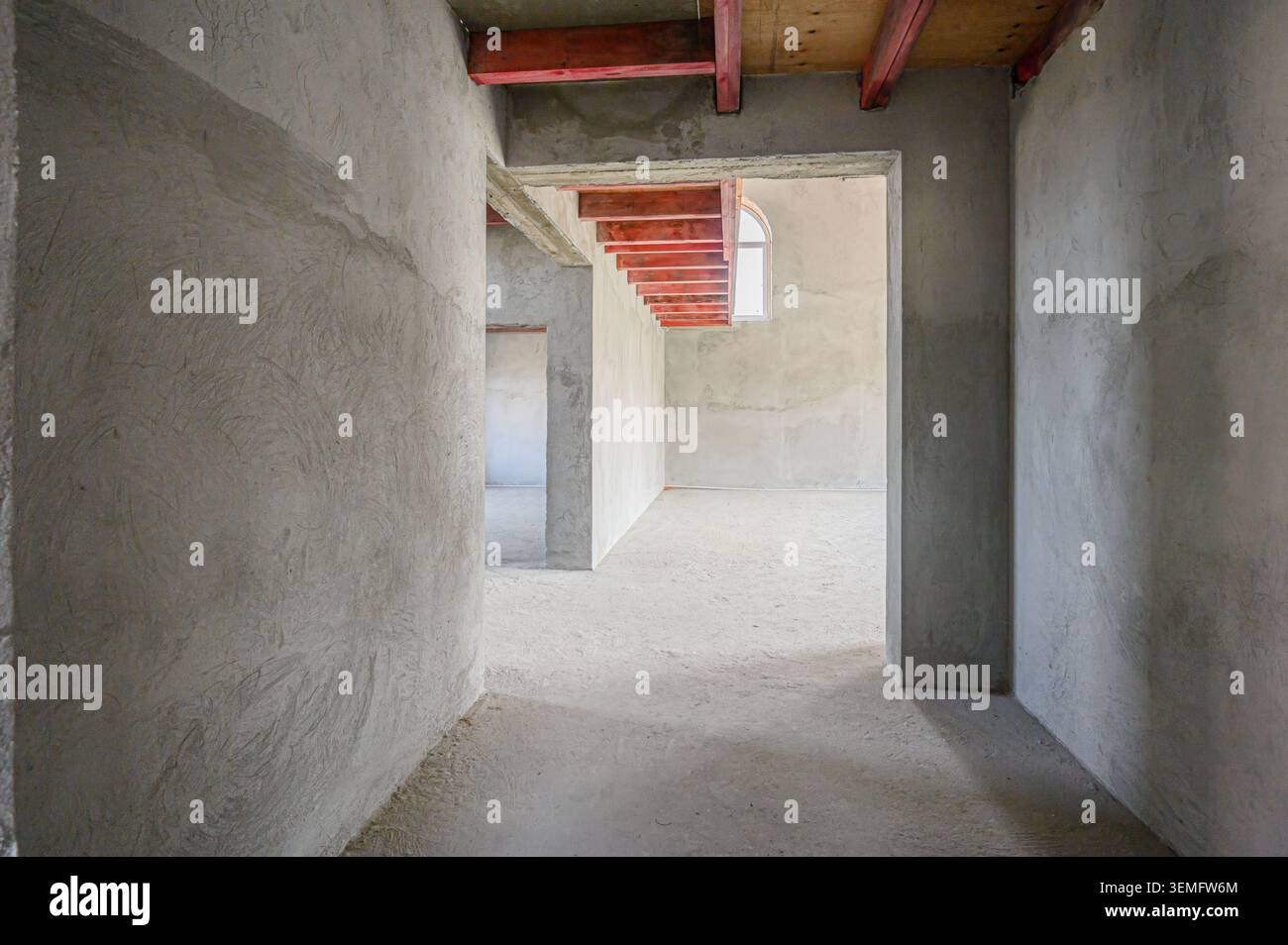 Geräumiges, unvollendetes Zimmer mit Betonwänden und Holzbalken. Es scheint sich im Bau oder in Renovierungsarbeiten zu befinden. Natürliches Licht strömt durch o Stockfoto
