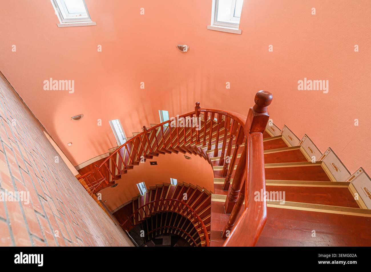 Hochwinkelaufnahme einer Wendeltreppe in einem Gebäude mit pfirsichfarbenen Wänden. Die Treppen sind aus Holz mit dekorativen Akzenten. Stockfoto