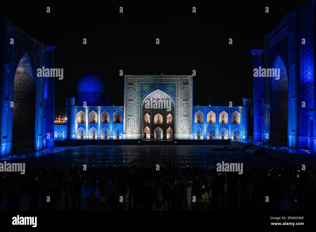 September 2026. Samarkand Usbekistan. Touristen laufen abends auf dem Registan-Platz in Samarkand, Usbekistan. Beleuchtete Madrasen. Gruppen Stockfoto