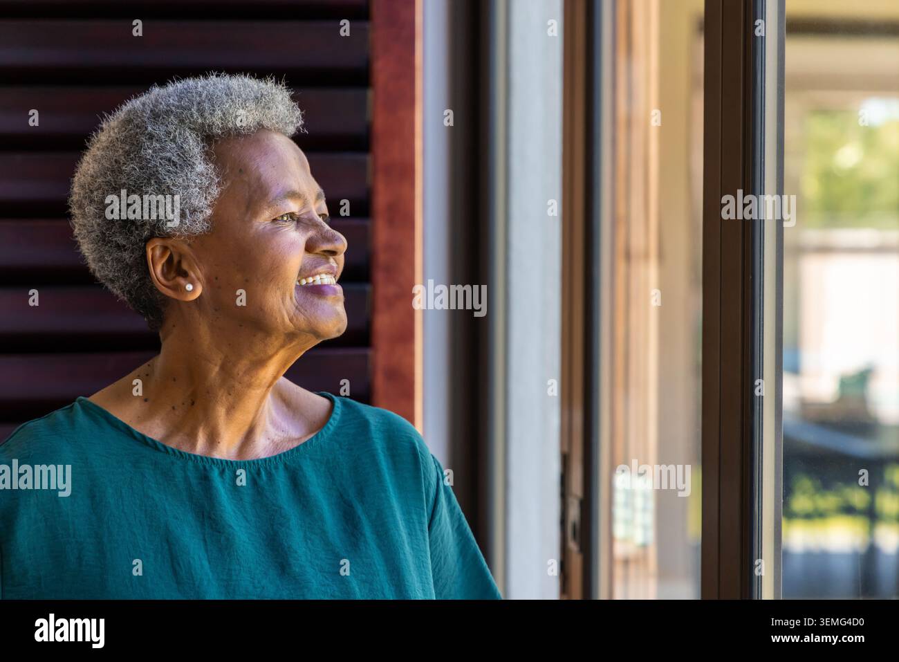 Eine ältere afroamerikanische Frau posiert vor einer Schiebetür zu Hause in der Nähe eines hölzernen Lamellen mit einer blauen Bluse Stockfoto
