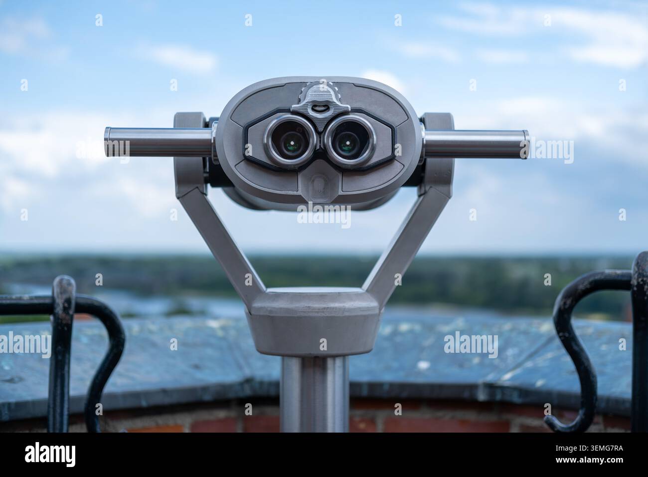 Das touristische Fernglas aus Metall steht auf einer Aussichtsplattform aus Backstein mit Blick auf den Fluss und die grüne Landschaft. Stockfoto