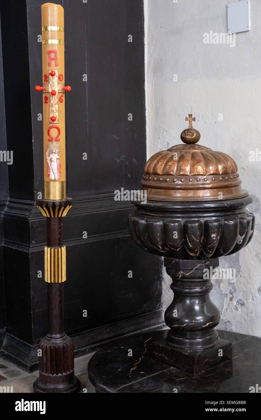 Liturgische Kerze und Marmortaufbecken stehen an einer Mauer in einer historischen Kirche. Stockfoto