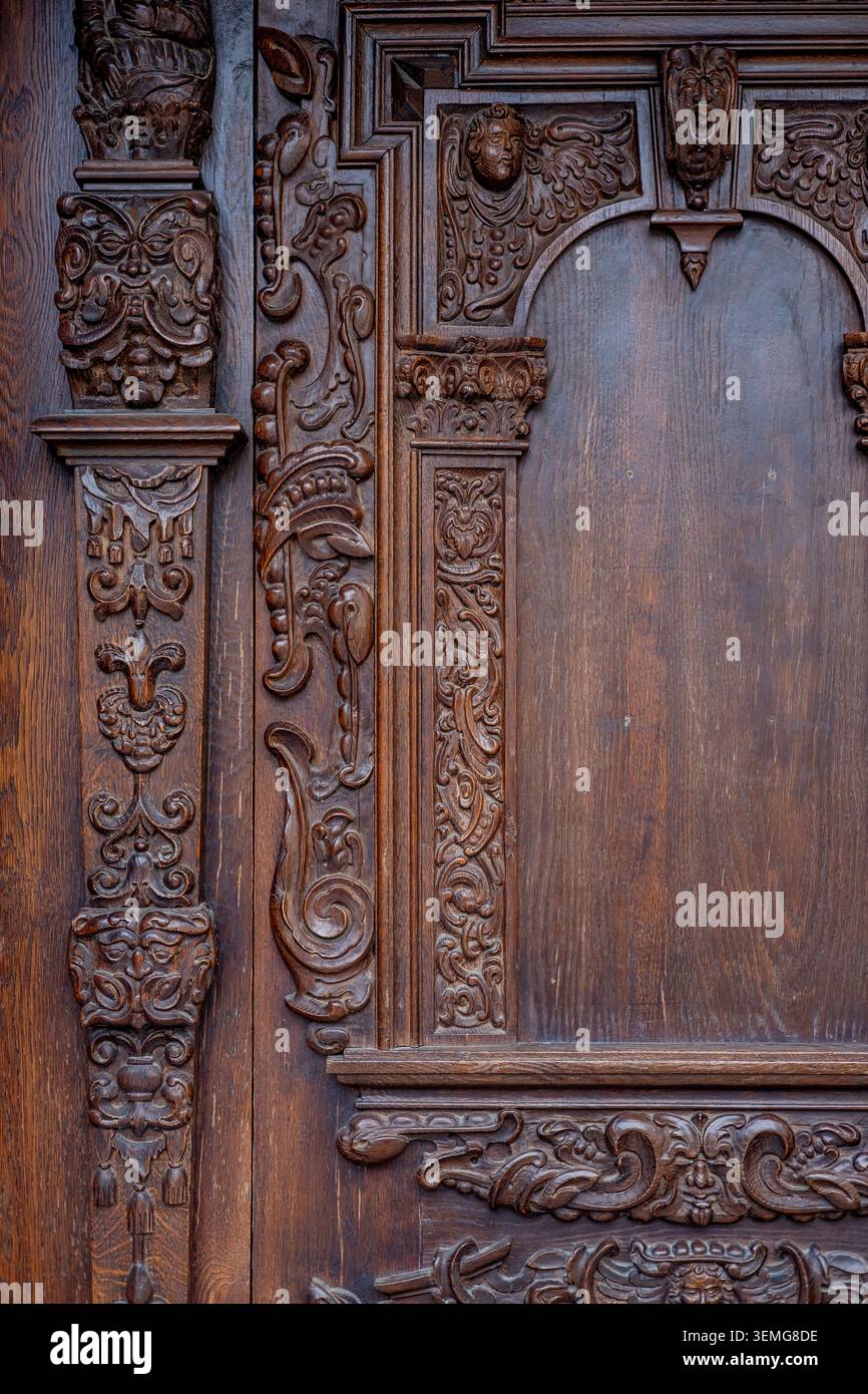 Der kunstvoll geschnitzte hölzerne Türbereich zeigt detaillierte Gesichter und Blumenmuster an einem historischen Eingang. Stockfoto
