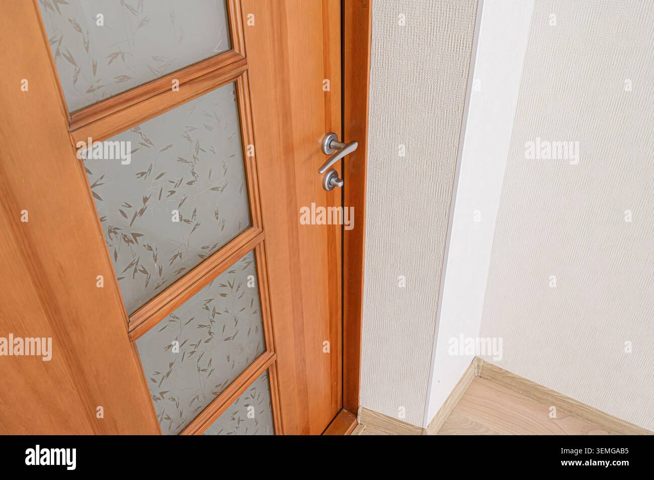 Teilweise offene Holztür mit Milchglaspaneelen, silbernem Griff und strukturierten Wänden Stockfoto