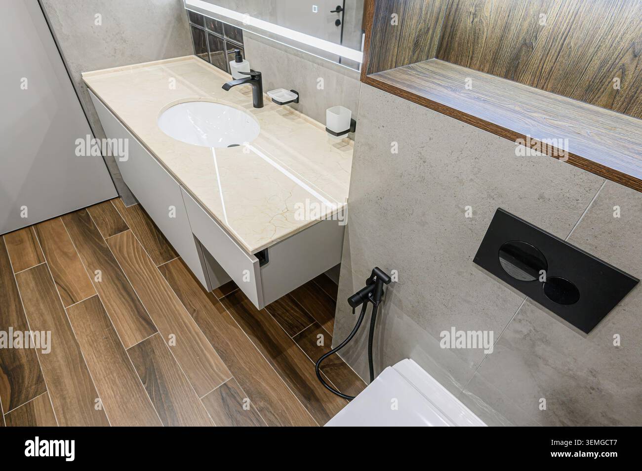 Modernes Bad mit beigefarbener Ablagefläche mit ovalem Waschbecken, schwarzem Wasserhahn und Fliesenboden in Holzoptik. Graue Fliesenwände runden das elegante Design ab Stockfoto