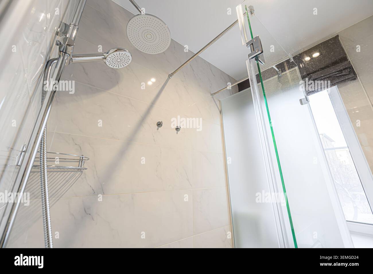 Helles Bad mit Dusche mit zwei Duschköpfen, Marmorfliesen und einer mattierten Glastür. Moderne und saubere Ästhetik. Stockfoto