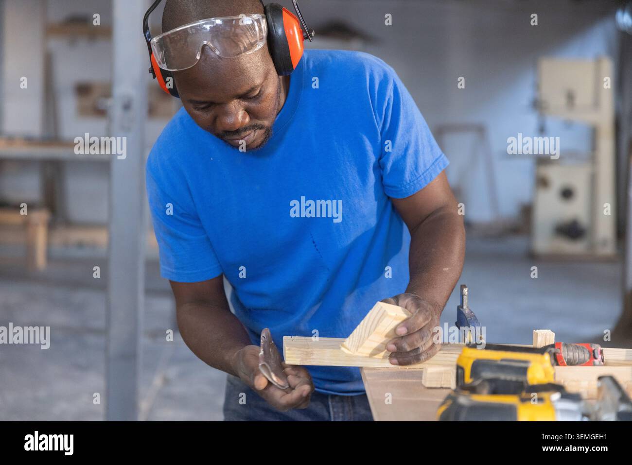 Ranghoher Afroamerikaner, der sich über die Bank in der Holzwerkstatt beugt und Holzblöcke mit Metallwerkzeug misst Stockfoto