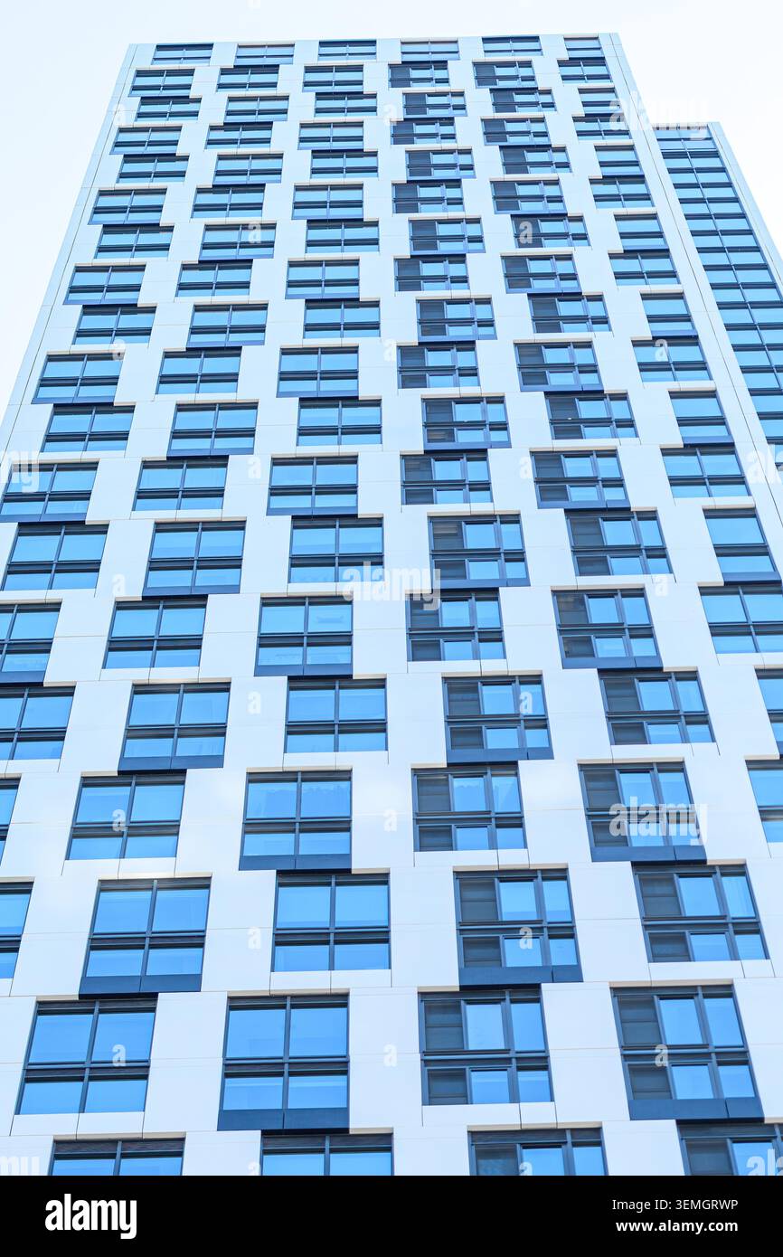 Moderne Hochhausfassade mit einem Gitter aus blau getönten Fenstern und weißen Verkleidungstafeln von unten. Stockfoto