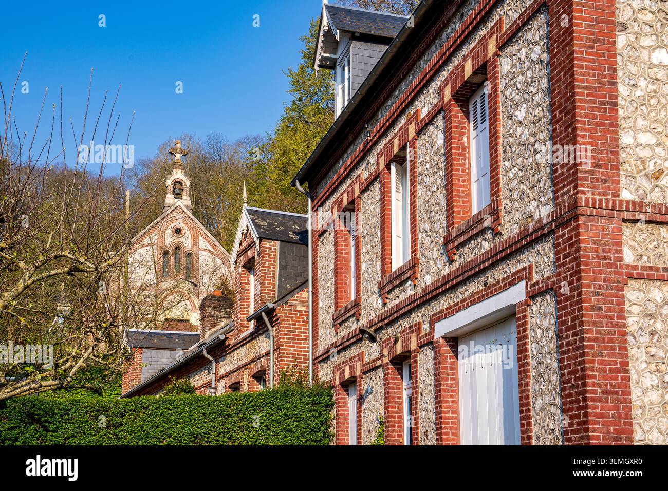 Charakteristische normannische Häuser aus Stein und roten Ziegeln weisen detaillierte Fassaden aus der Epoche auf. Im Hintergrund taucht eine bezaubernde Steinkapelle auf Stockfoto