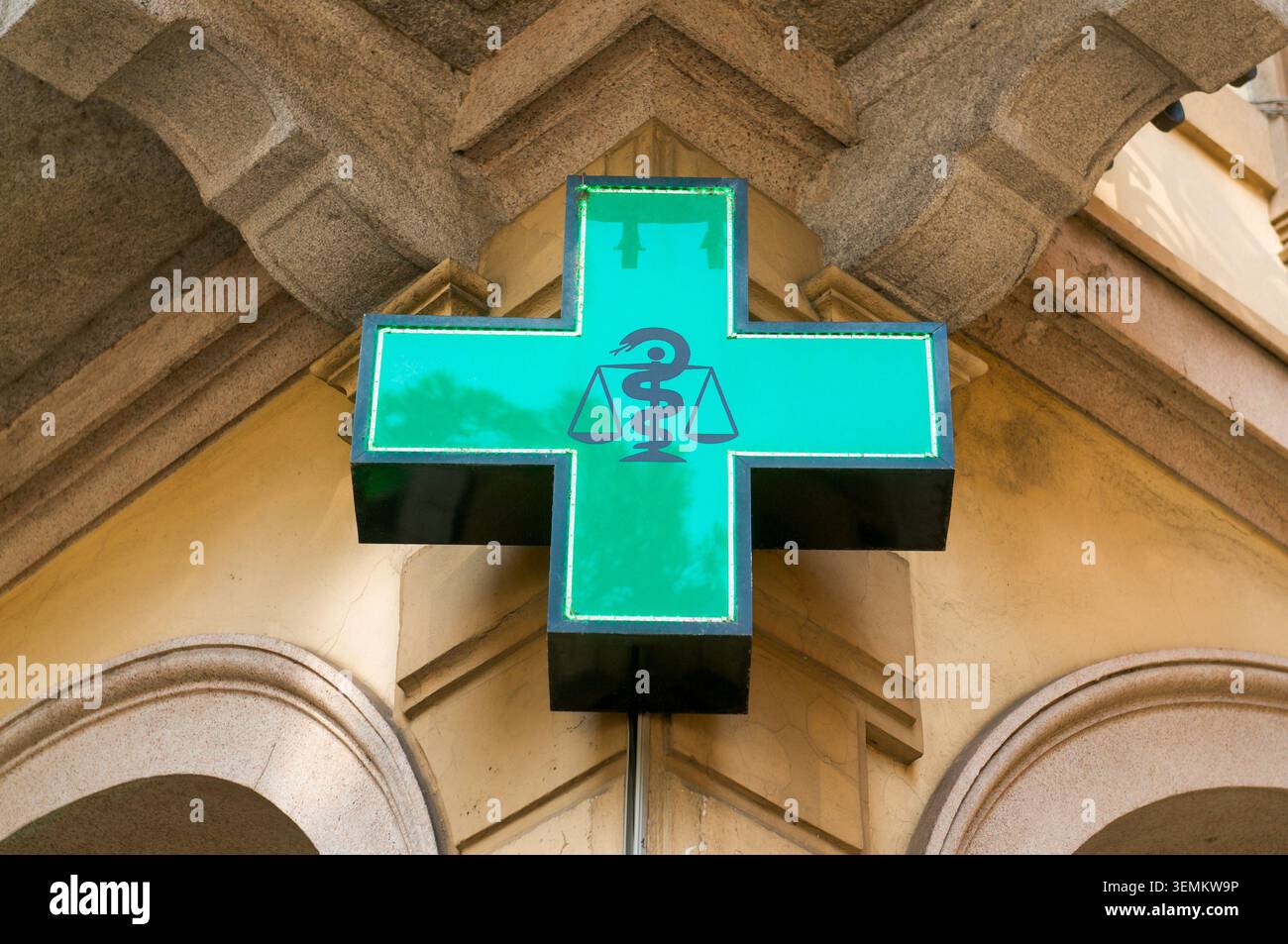 Nahaufnahme eines leuchtend grünen Apotheken-LED-Kreuzschilds, das vor einem traditionellen Steinpalast-Geschäft montiert ist. Gesundheitswesen, medizinische Dienstleistungen und Stockfoto