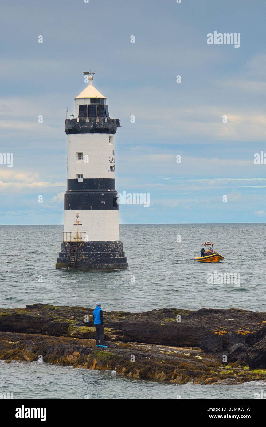 14. Mai 2026, angleseyTrwyn du Lighthouse in Penmon Point, Anglesey, mit seinen schwarz-weißen Streifen mit einem kleinen gelben Boot auf dem Meer und männlich Stockfoto
