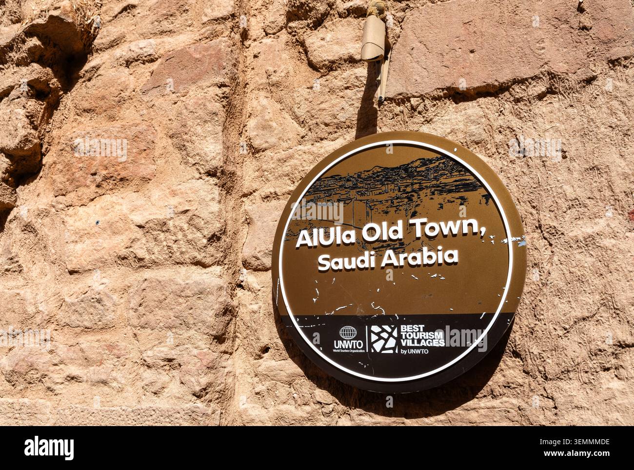 Alula, Saudi-Arabien - 15. Februar 2026: Eine Gedenktafel an einer Lehmziegelmauer, die Alula Altstadt als eines der besten Tourismusdörfer der UNWTO in Saudi-Arabien identifiziert. Stockfoto