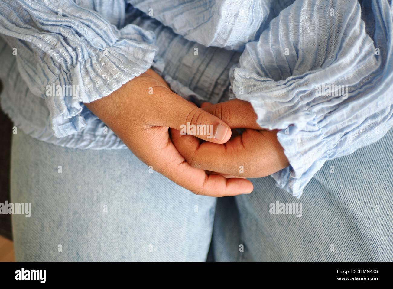 Zwei Hände verschließen sich sanft, während ein Kind still sitzt Stockfoto