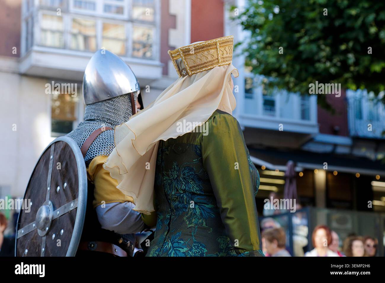 Zwei mittelalterliche Reenactoren: Ein Krieger mit Stahlhelm, Kettenhemd, gelber Tunika und rundem Holzschild, zusammen mit einer Frau in einem kunstvollen Gr Stockfoto
