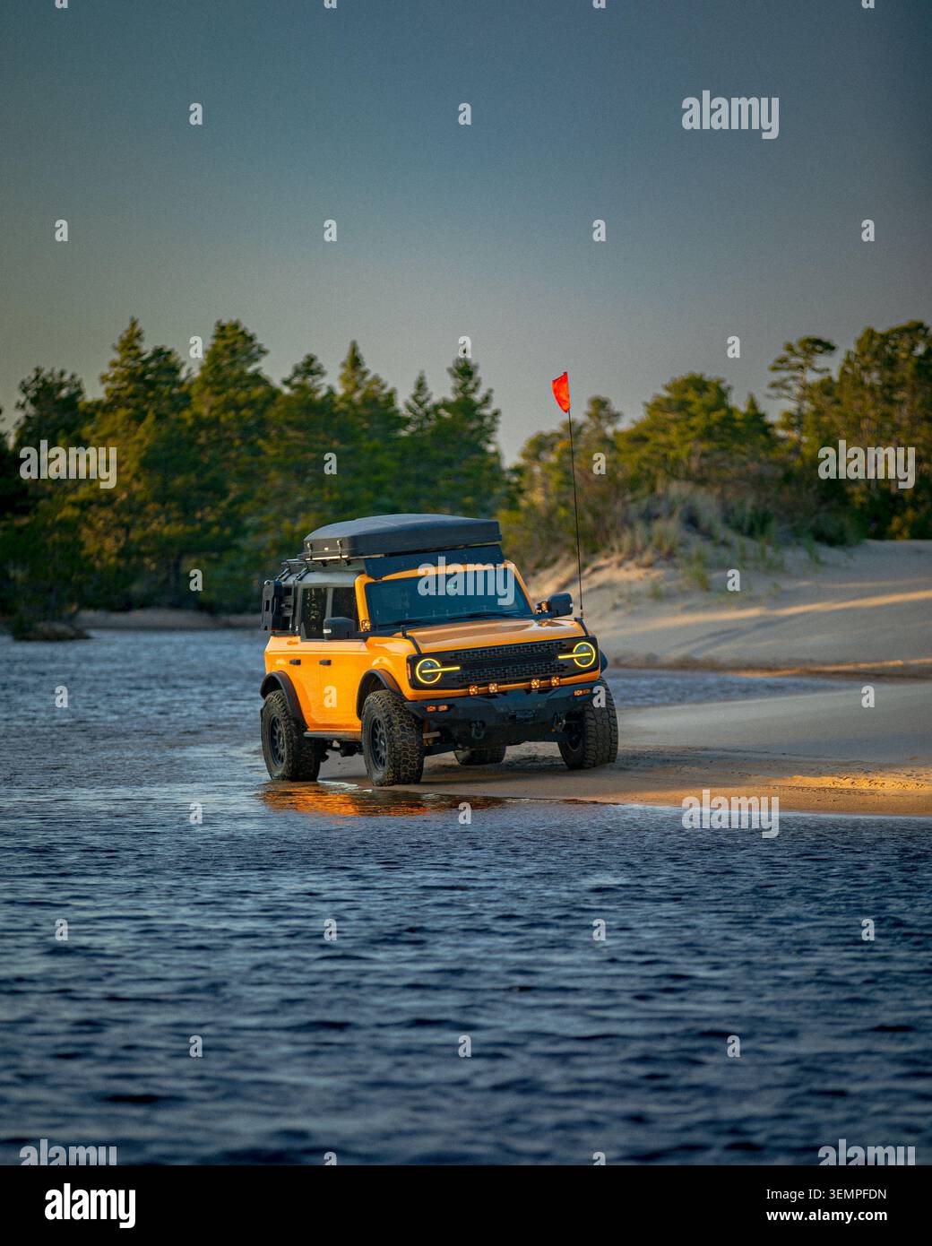 Orangefarbenes Geländefahrzeug, das aus dem Wasser auf einen Strand fährt Stockfoto
