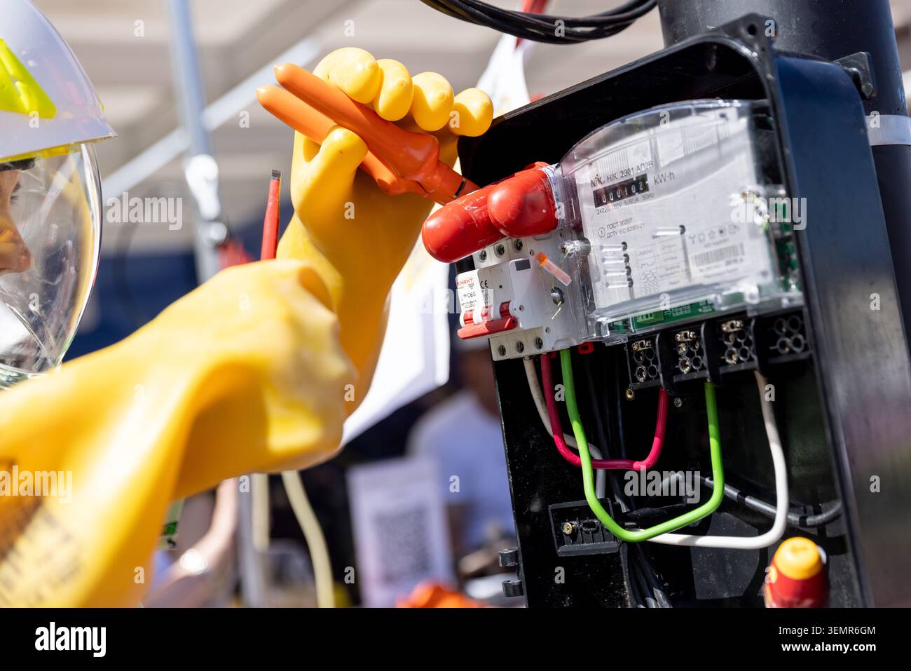 Professioneller Elektriker, der mit isolierten Werkzeugen in einer elektrischen Schalttafel arbeitet. Nahaufnahme der Hände in gelben Sicherheitshandschuhen, die ein p Stockfoto