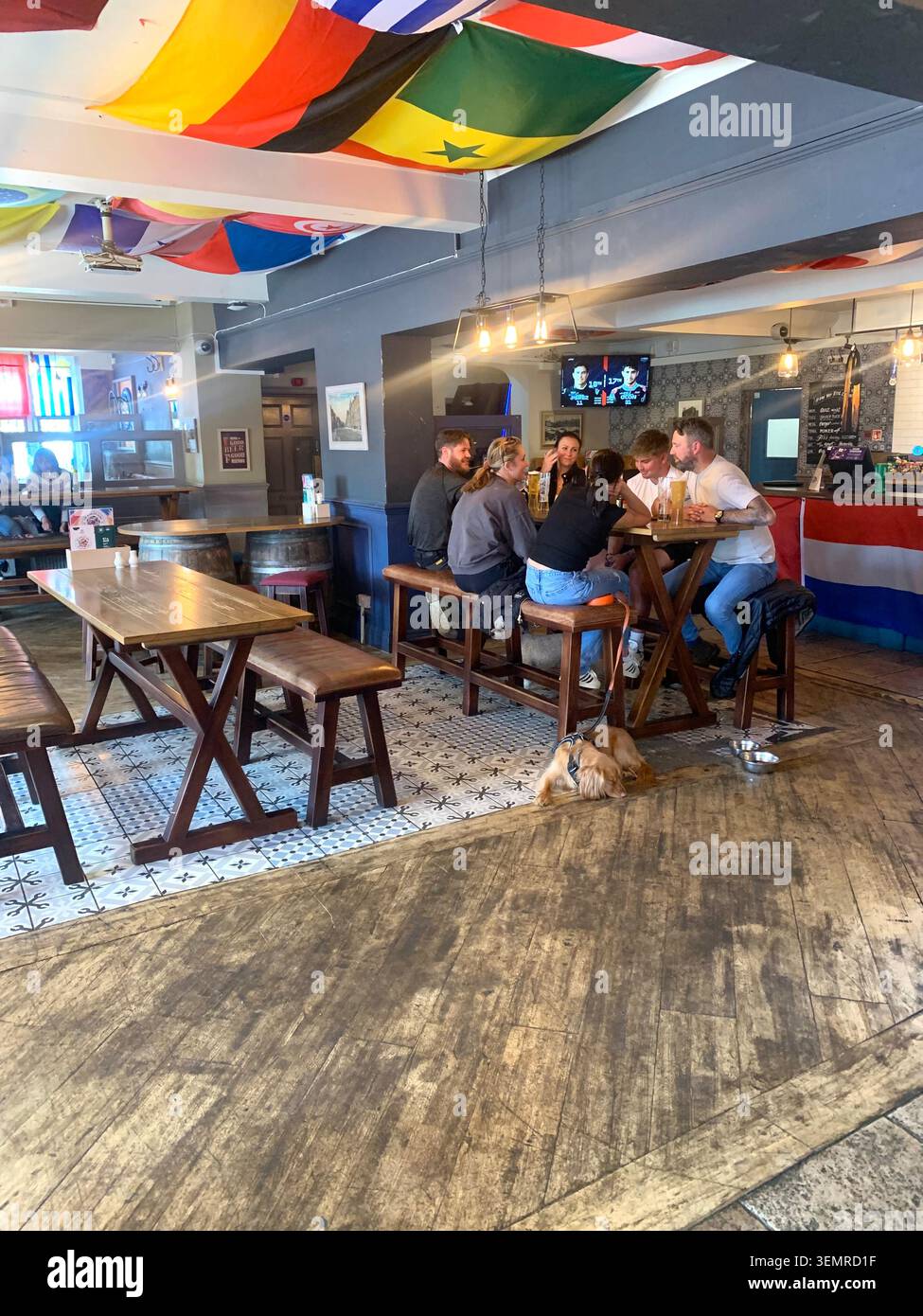 Freunde versammeln sich an einem Tisch in einem lebhaften Pub, der mit internationalen Flaggen dekoriert ist, in einem warmen Trompetenlokal Weston Favell Northampton England - Smartphone-aufgenommenes Stockfoto