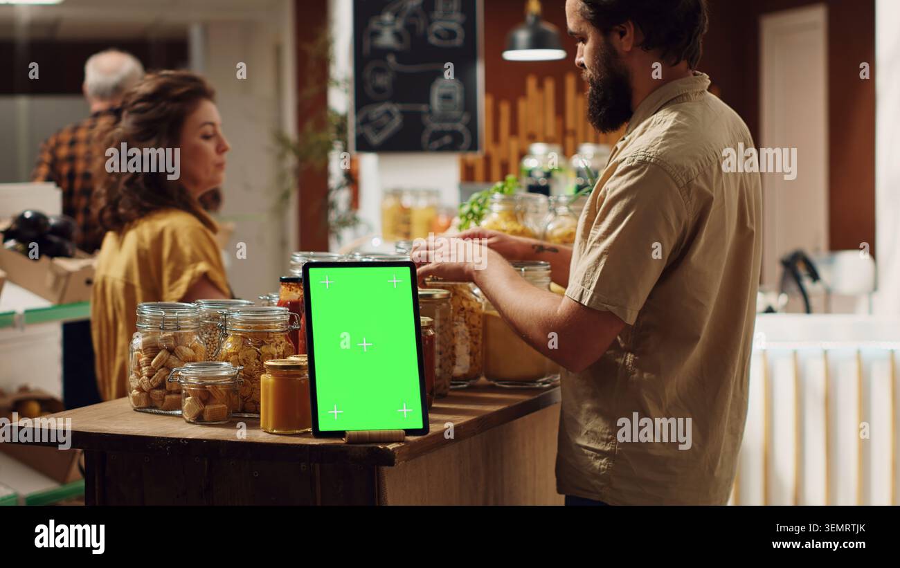 Kundengeschäfte neben Chroma Key Tablet mit Kopierraum als Werbezeichen im Null-Abfall-Supermarkt, mit Werbeanzeige auf dem Green-Screen-Gerät im Lebensmittelgeschäft mit Produkten in umweltfreundlichen Verpackungen Stockfoto